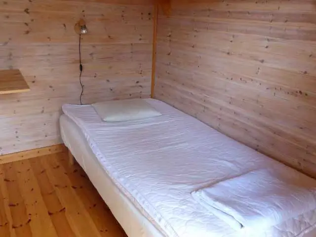 Enkelt sovrum i trästuga med bekväm säng och träpaneler, lugnt boende nära Åsnens Nationalpark i Småland.